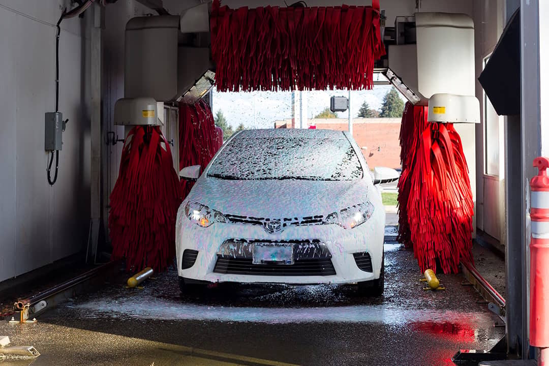 A white car covered in soap suds as it passes through a car wash lane.